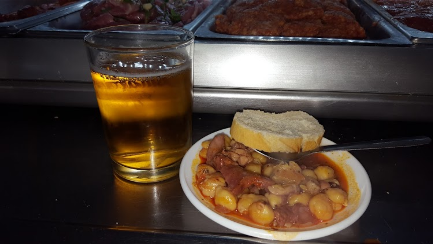 Vaso de cerveza junto a una tapa con garbanzos y pan sobre la barra